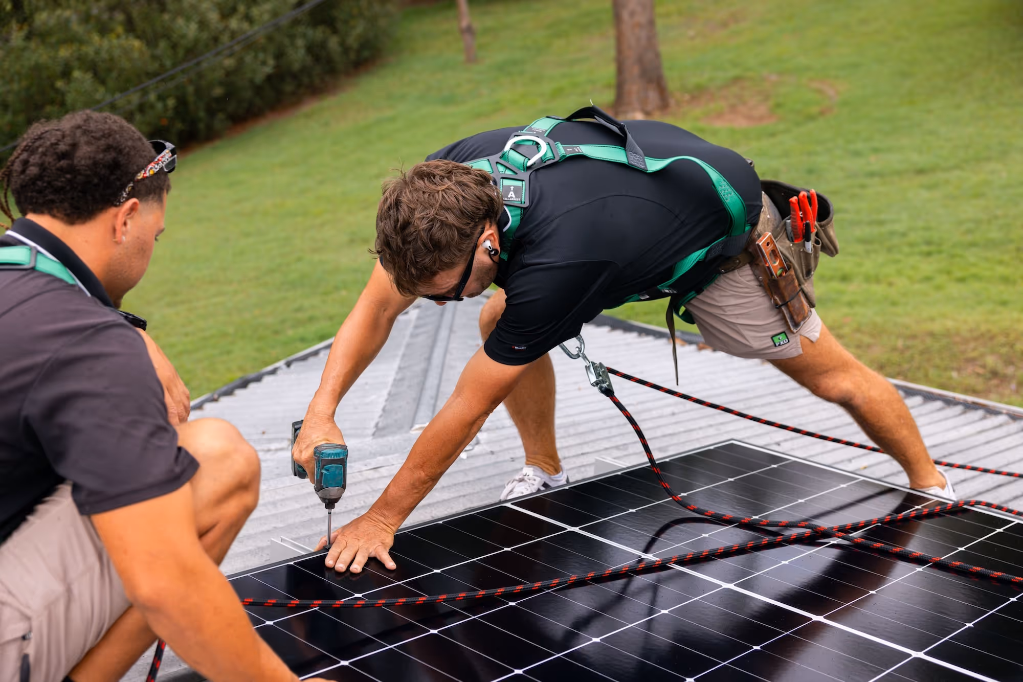 Two LMS Electrical installers securing solar panels to a corrugated roof with precision tools and full safety gear.
