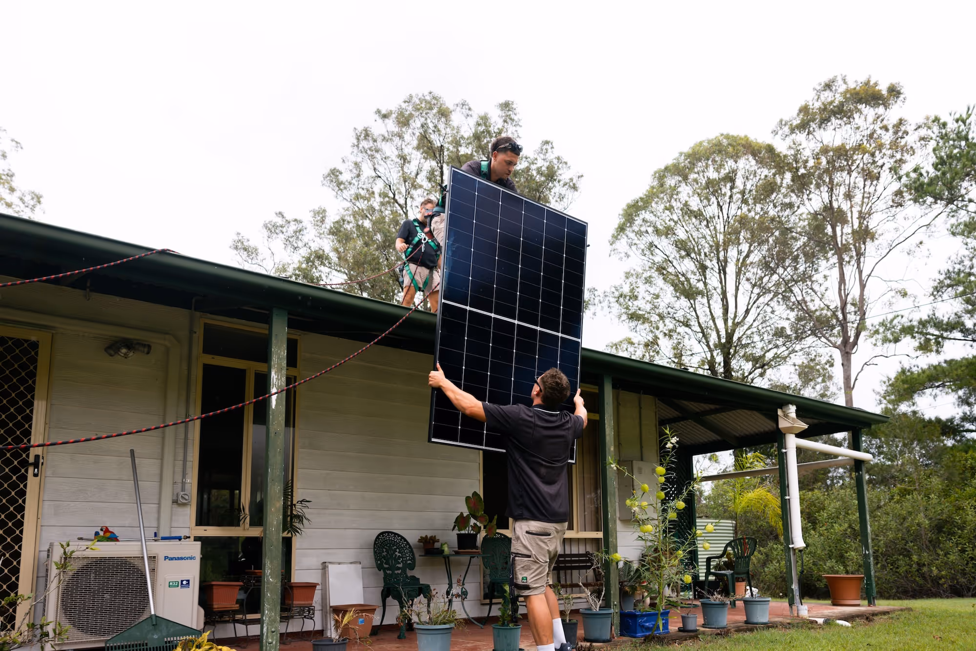 LMS Electrical team carefully lifting a solar panel onto a residential roof.