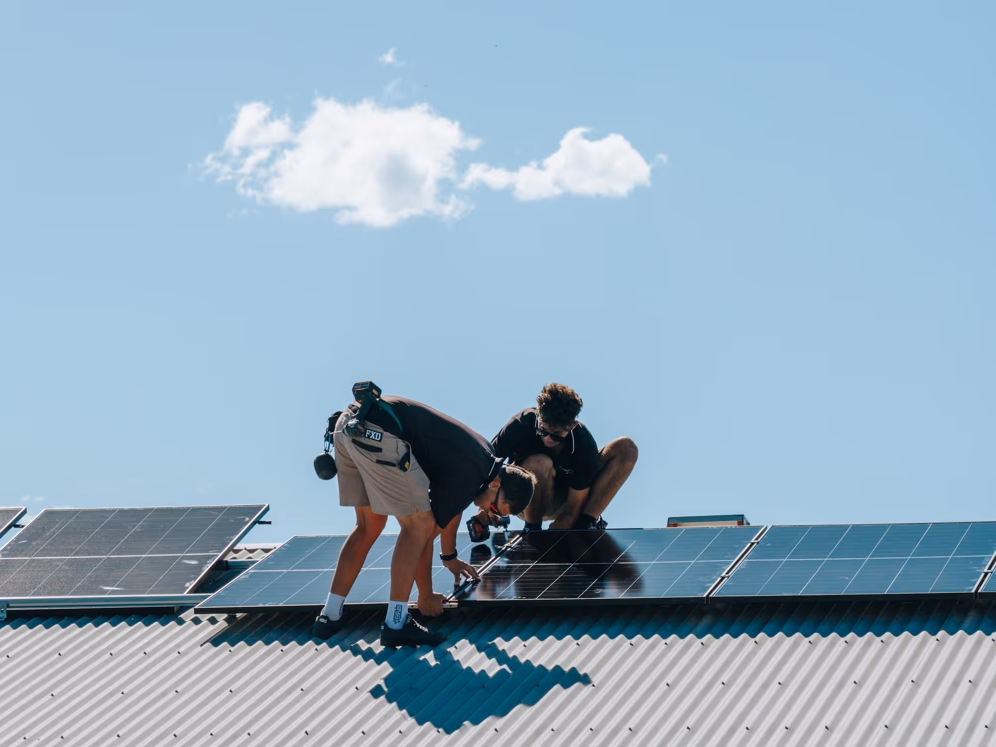 LMS Electrical team securing solar panels to a corrugated iron roof under a clear blue sky.