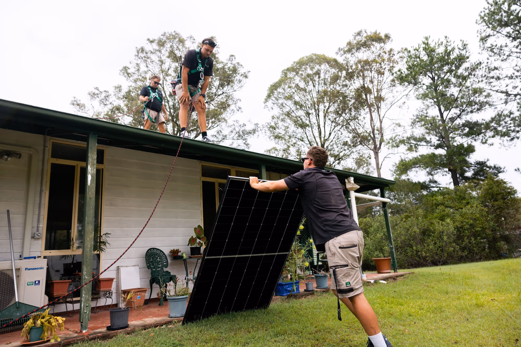 LMS Electrical installers coordinating a safe manual lift of a solar panel from the ground to the roof team.